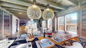Un comedor moderno con una mesa de madera preparada para una comida, ventanas amplias y una chimenea.