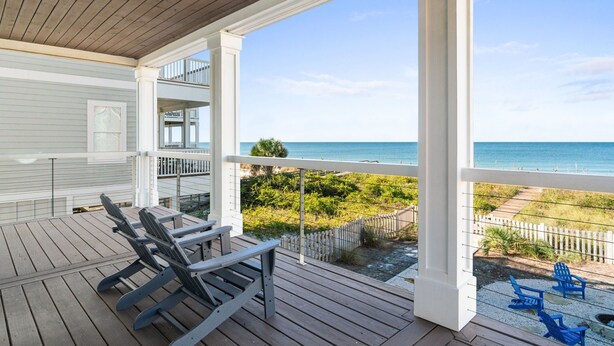 A wooden deck with two Adirondack chairs facing a beach view.