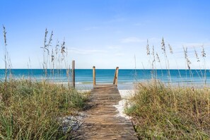 Un sentier en bois mène à une plage, de part et d’autre duquel s’étend une végétation luxuriante.