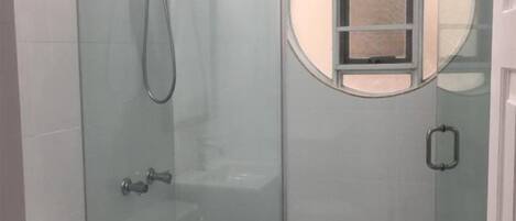 Um banheiro moderno com chuveiro em box de vidro, vaso sanitário e toucador com espelho.