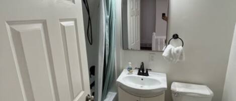 A bathroom with a white door, a shower, a sink, and a toilet.