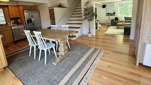 A modern kitchen with wooden cabinets, a stainless steel refrigerator, and a dining area with a wooden table and white chairs.