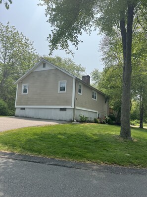 A two-story house with a front yard, a driveway, and a large tree.