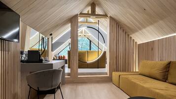 Un dormitorio tipo loft moderno con techo inclinado, una lámpara circular en el centro, un sofá, una mesa de comedor y un televisor.