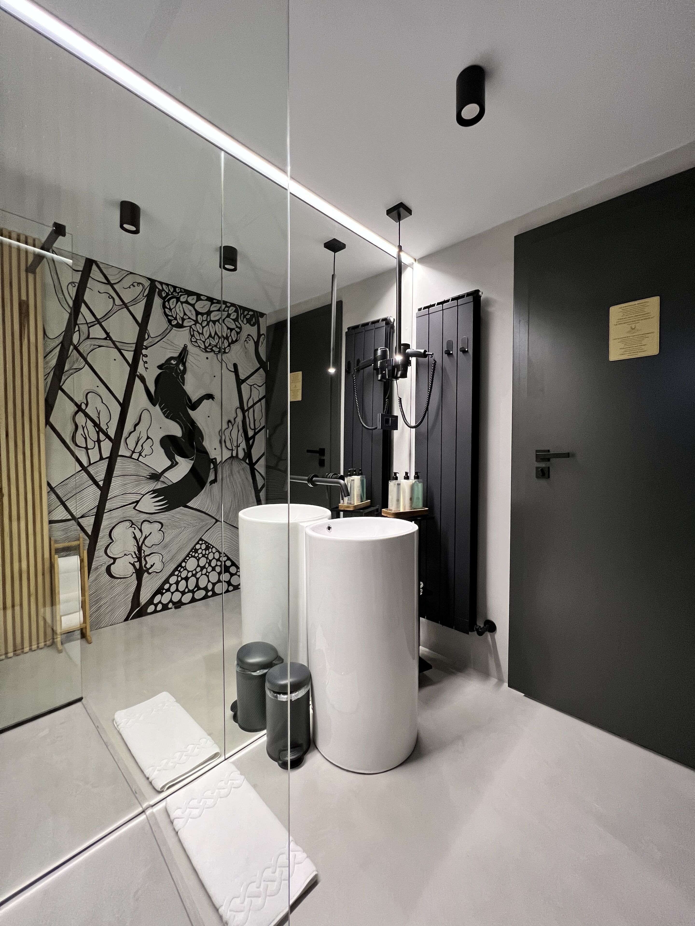 Un baño moderno con dos lavamanos, un espejo grande y un mural geométrico en la pared.