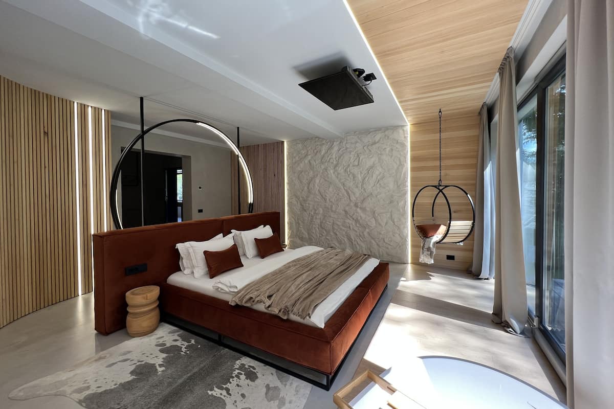 A modern bedroom with a large bed, a hanging chair, and a view of the outdoors.