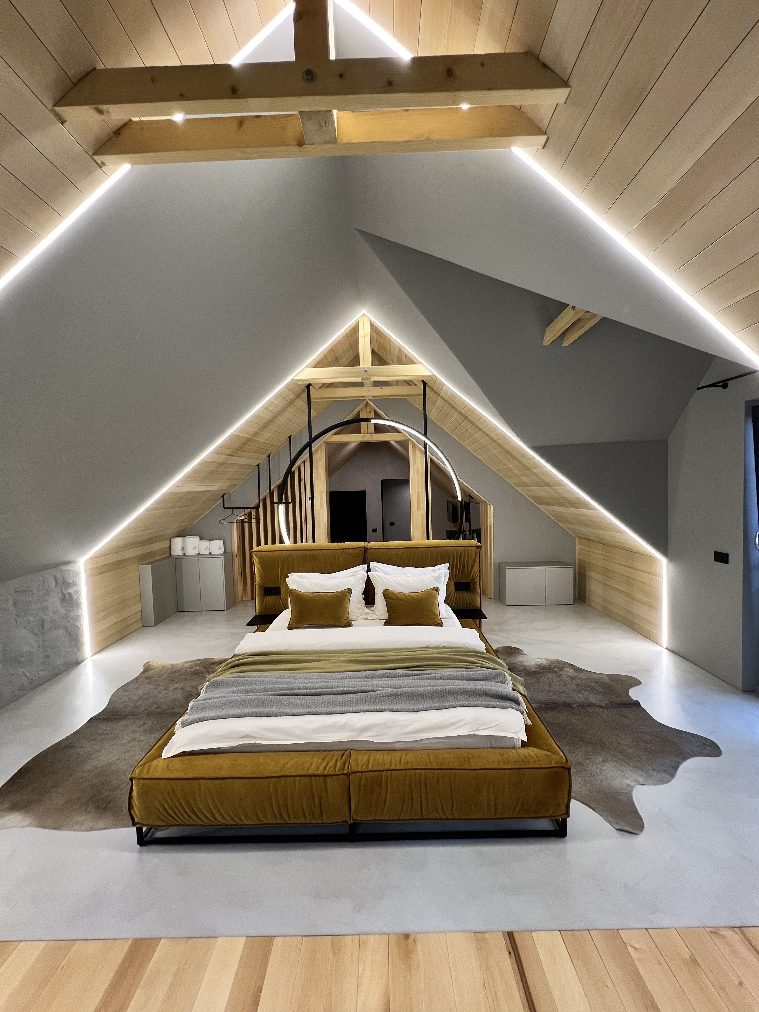 A modern loft bedroom with a sloped ceiling, a central bed, and a staircase leading to an upper level.