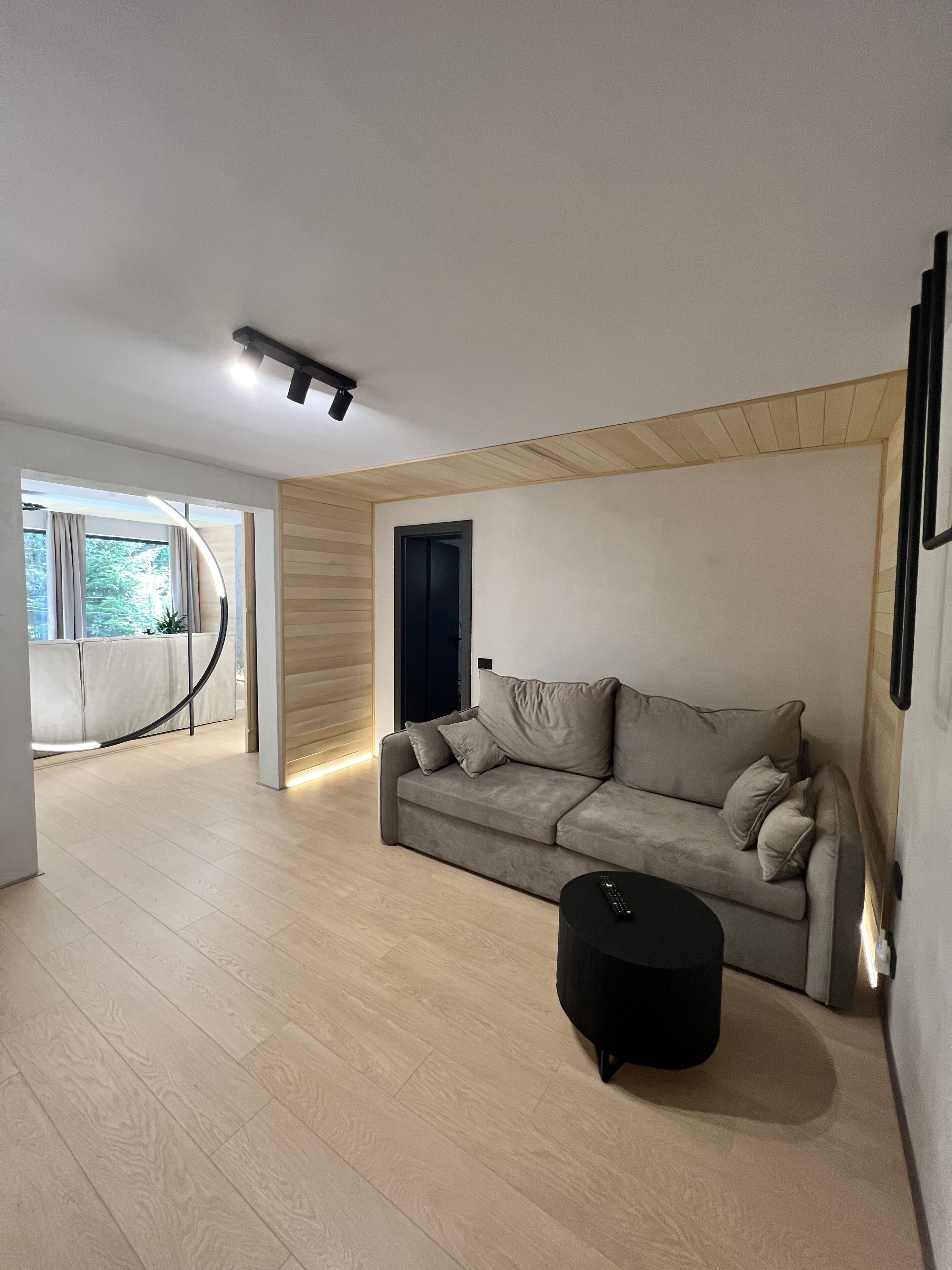 A modern living room with a grey sofa, a black ottoman, and a wooden accent wall.
