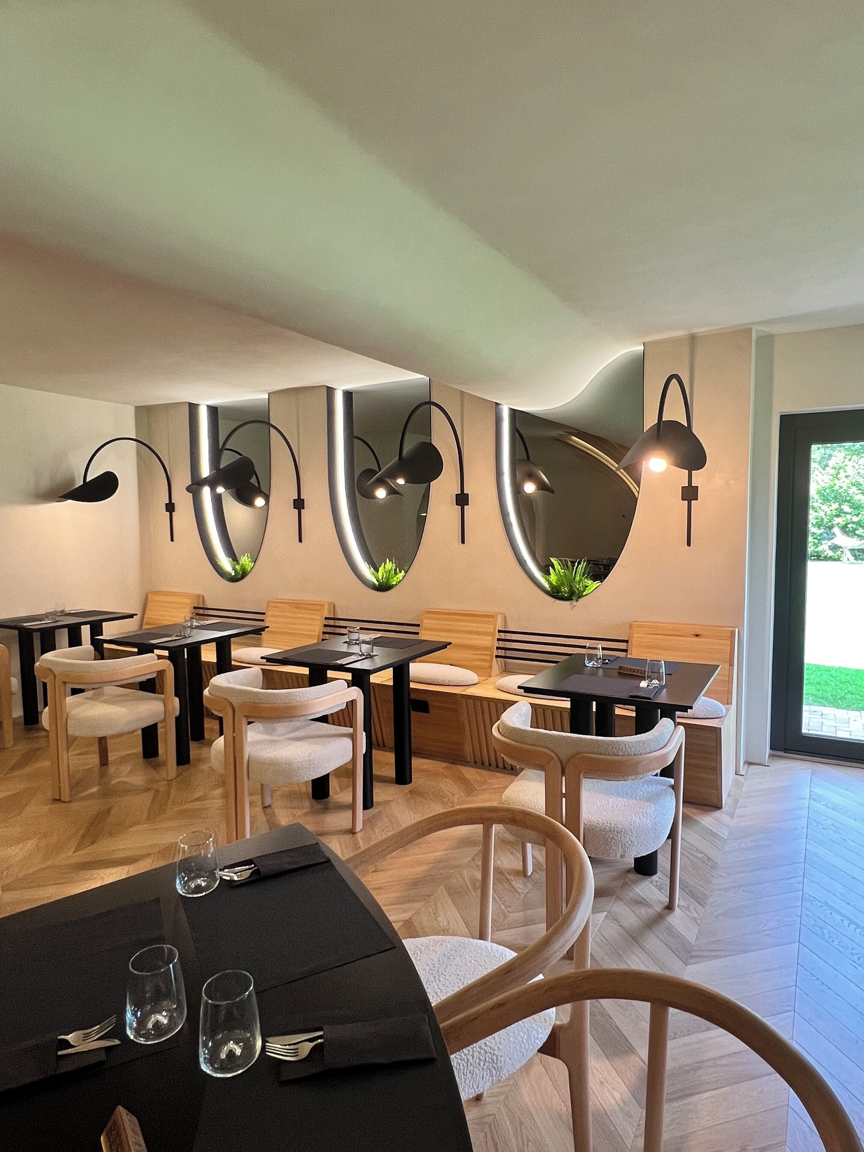 A modern dining area with wooden tables and chairs, black tablecloths, and wall-mounted lighting fixtures.
