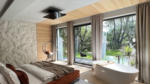 A modern bedroom with a large bed, a bathtub, and a view of the outdoors. - Garden Retreat  (Bran)