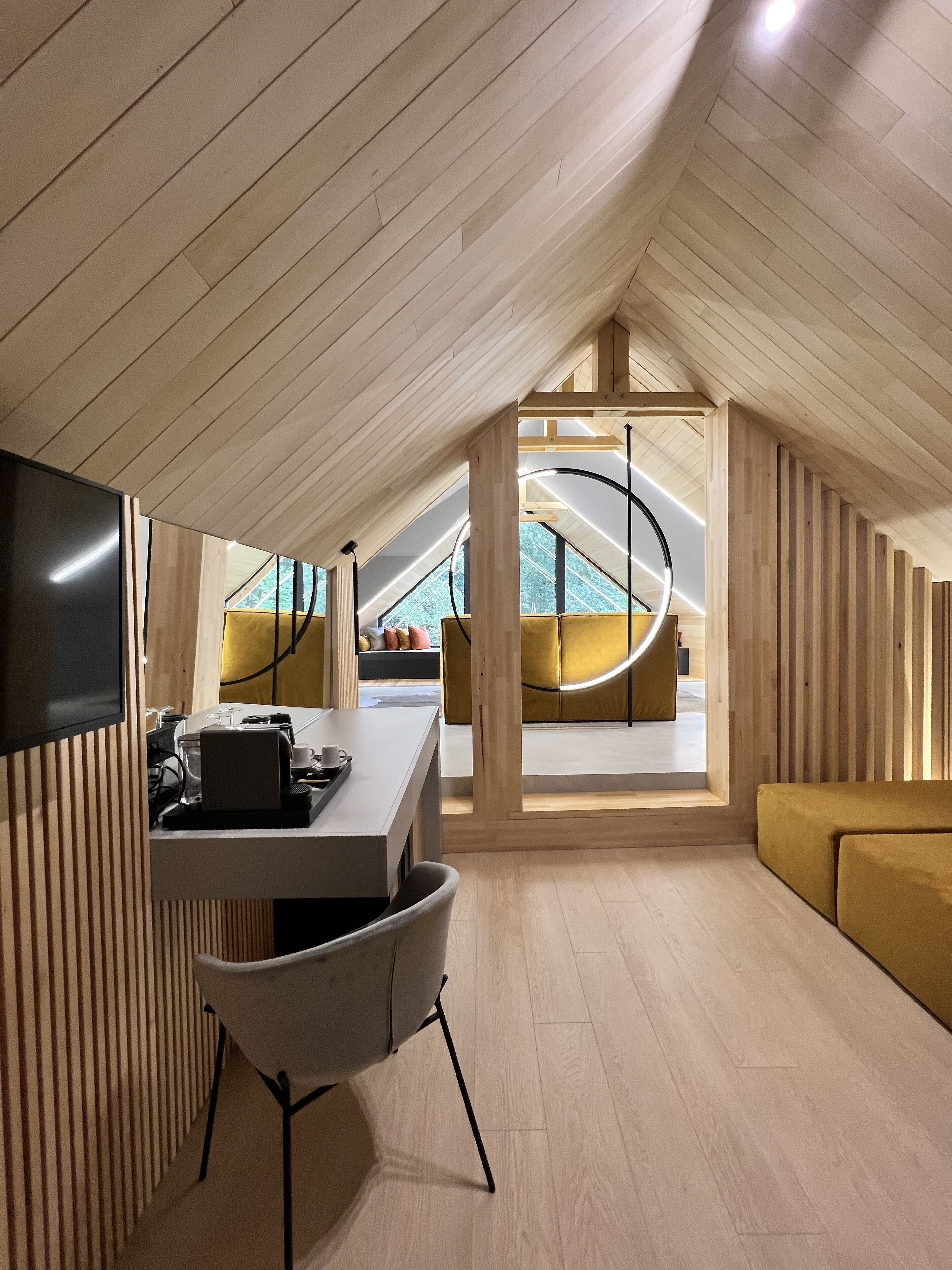 Un loft moderno con techo alto, listones de madera, zona de comedor con mesa y sillas, sofá y un ventanal con vistas al exterior.
