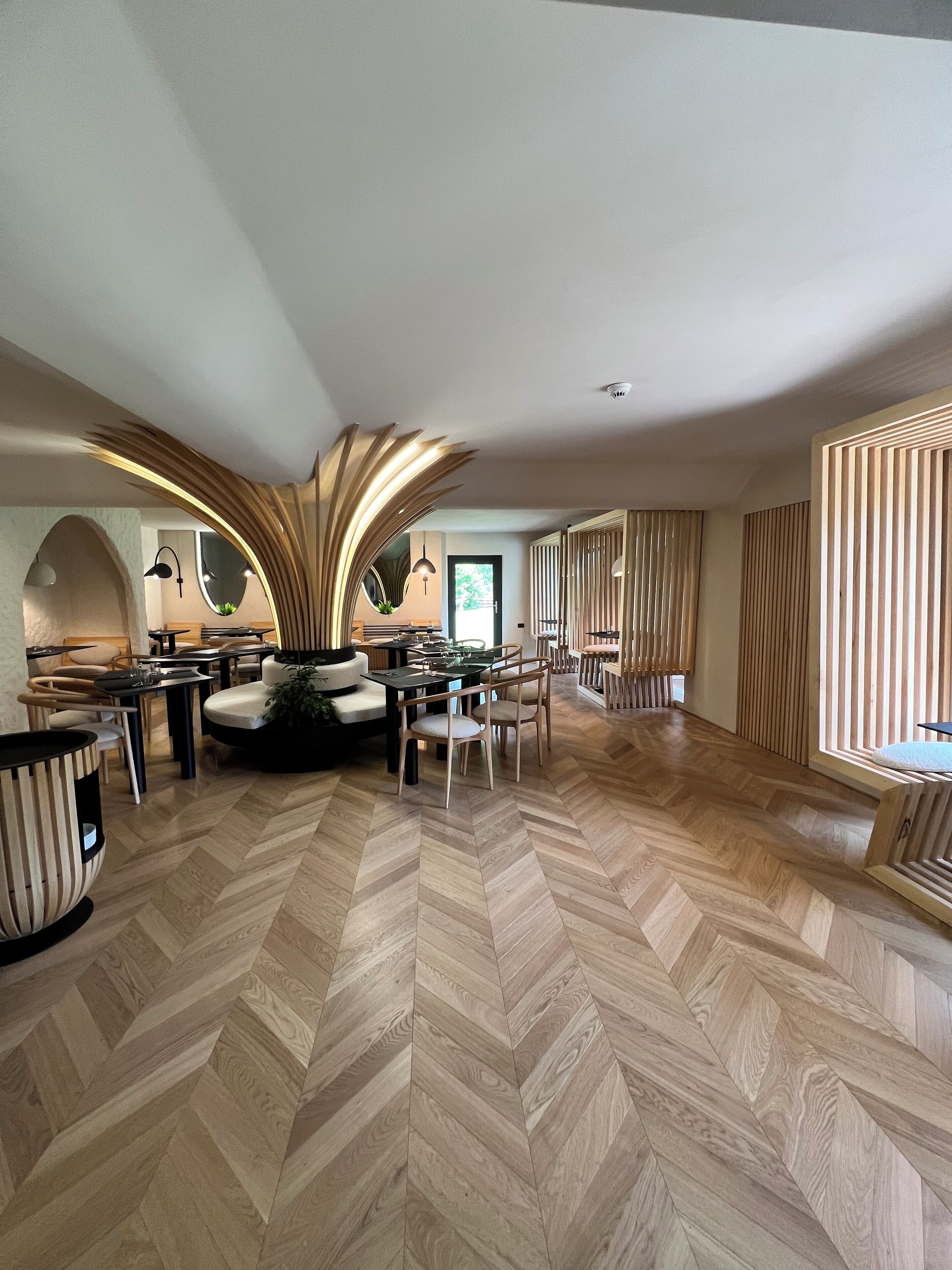 Un interior espacioso y moderno con suelo de madera en espiga, muebles contemporáneos y una zona de estar central con una lámpara curva y distintiva.