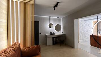 A modern living room with a brown sofa, a wooden slatted wall, a desk with two round mirrors, and a ceiling light fixture.