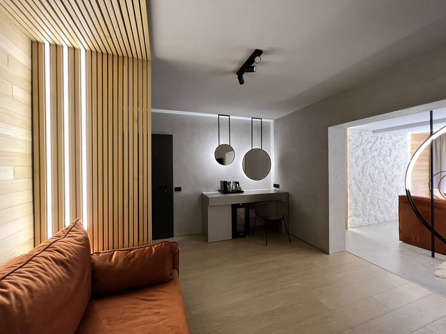 A modern living room with a brown sofa, a wooden slatted wall, a desk with two round mirrors, and a ceiling light fixture.