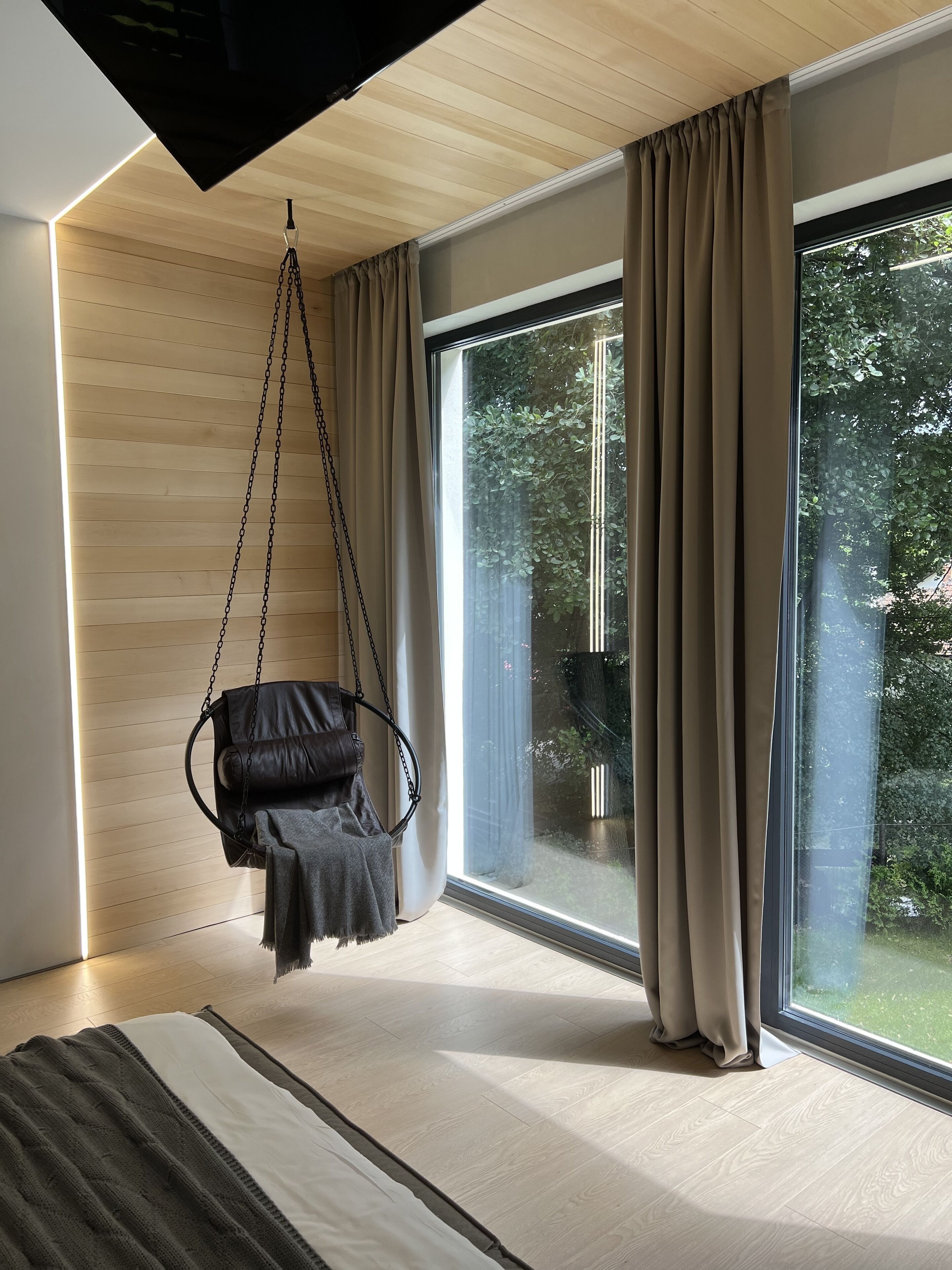 Una habitación moderna con una silla colgante, ventanas amplias y vistas a la vegetación.