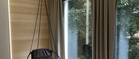 Una habitación moderna con una silla colgante, ventanas amplias y vistas a la vegetación.