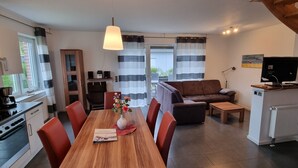 A modern kitchen with a dining table, chairs, and a vase with flowers. There is a sofa and a TV in the living area.