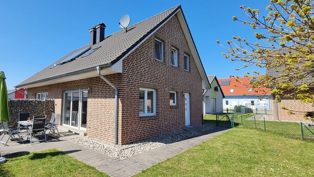 A two-story house with a brick exterior, a sloped roof, and a patio area with outdoor furniture.