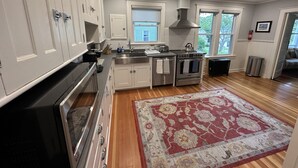 A modern kitchen with white cabinets, stainless steel appliances, and a red patterned rug. - Beautifully Remodeled Family Size Apartment, Ideal for Downtown & Beach Getaway (Westerly)