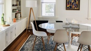 A modern dining area with a round glass table, white chairs, a blue patterned rug, and a ceiling fan. - Beautifully Remodeled Family Size Apartment, Ideal for Downtown & Beach Getaway (Westerly)