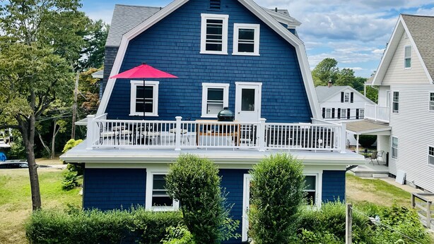 A two-story house with a blue exterior, white trim, and a balcony with a red umbrella. - Beautifully Remodeled Family Size Apartment, Ideal for Downtown & Beach Getaway (Westerly)