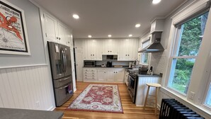 A modern kitchen with white cabinets, stainless steel appliances, and a wooden floor. - Beautifully Remodeled Family Size Apartment, Ideal for Downtown & Beach Getaway (Westerly)