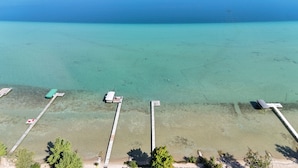 Eine Vogelperspektive zeigt einen Strand mit klarem türkisblauem Wasser, einen hölzernen Steg und einen kleinen Bootsanleger.