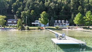 A lakeside property with a dock, clear water, and a house with a porch.