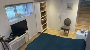 Ein Schlafzimmer mit Bett, Fernseher, Bücherregal, Sessel und Fenster.