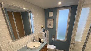 Ein Badezimmer mit einem weißen Waschbecken, einem Holz-Waschtisch, einer Toilette und einer Duschkabine.