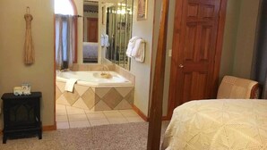 Un dormitorio con cama, puerta de madera, baño con bañera y espejo.