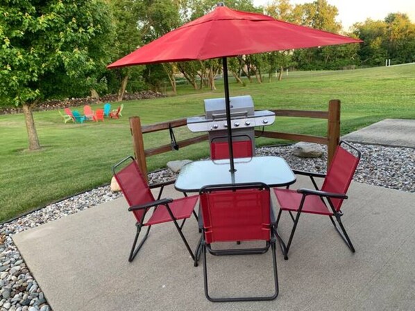 Eine Terrassenanlage im Freien mit Grill, roten Stühlen und einem roten Sonnenschirm.