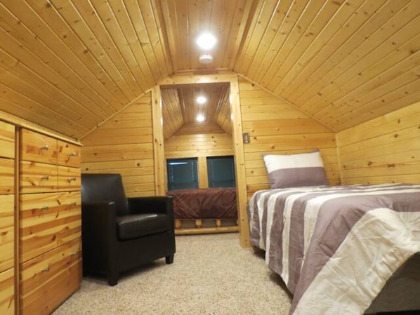 A cozy wooden cabin room with a bed, a chair, and a small desk.