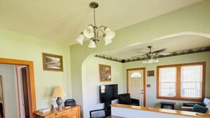 A dining area with a wooden table and chairs, a wooden bench with a lamp, a ceiling fan, and a television on a stand. - Countryside Escape - 10 minutes from downtown South Haven! (Bangor)