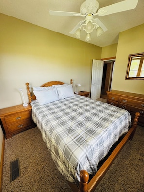 Un dormitorio con cama, mesitas de noche, cómoda, ventilador de techo y puerta.