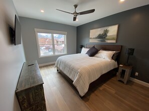 A bedroom with a bed, a ceiling fan, a nightstand, a lamp, a window, and a painting on the wall.