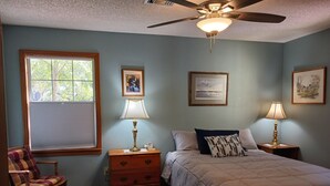 Una camera da letto con un letto, due comodini, una sedia, una finestra e ventilatori a soffitto.