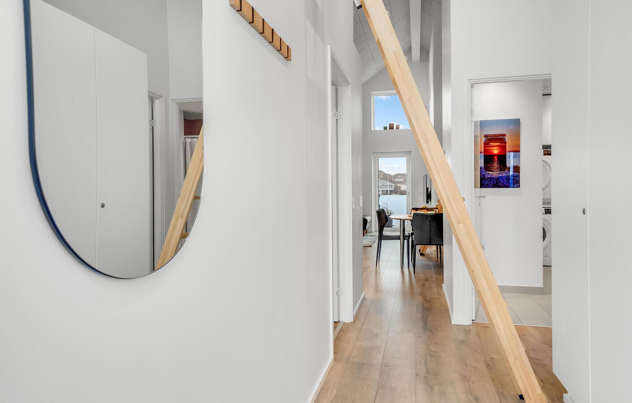 A modern interior with a wooden staircase, a round mirror, and a dining area with a view of the outdoors.