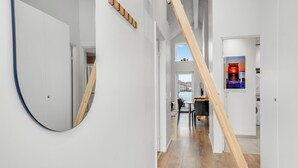 A modern interior with a wooden staircase, a round mirror, and a dining area with a view of the outdoors. - Amazing apartment in Ringkøbing (Ringkøbing)