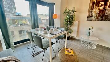 Un salon moderne comprenant un coin repas, de grandes fenêtres, une plante en pot et une œuvre d’art encadrée.