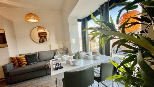 Una sala de estar moderna con un sofá, una mesa de comedor, sillas y un ventanal con vistas a edificios.