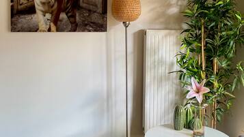 Une pièce décorée d’un tableau représentant un tigre, avec un lampadaire, une plante en pot, un vase rempli de fleurs et une table ronde sur laquelle se trouve un panier en fil de fer.