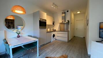 Een praktische keuken met een wasmachine, een eethoek met een tafel en stoelen, en een gezellig zithoekje met vloerkleed.