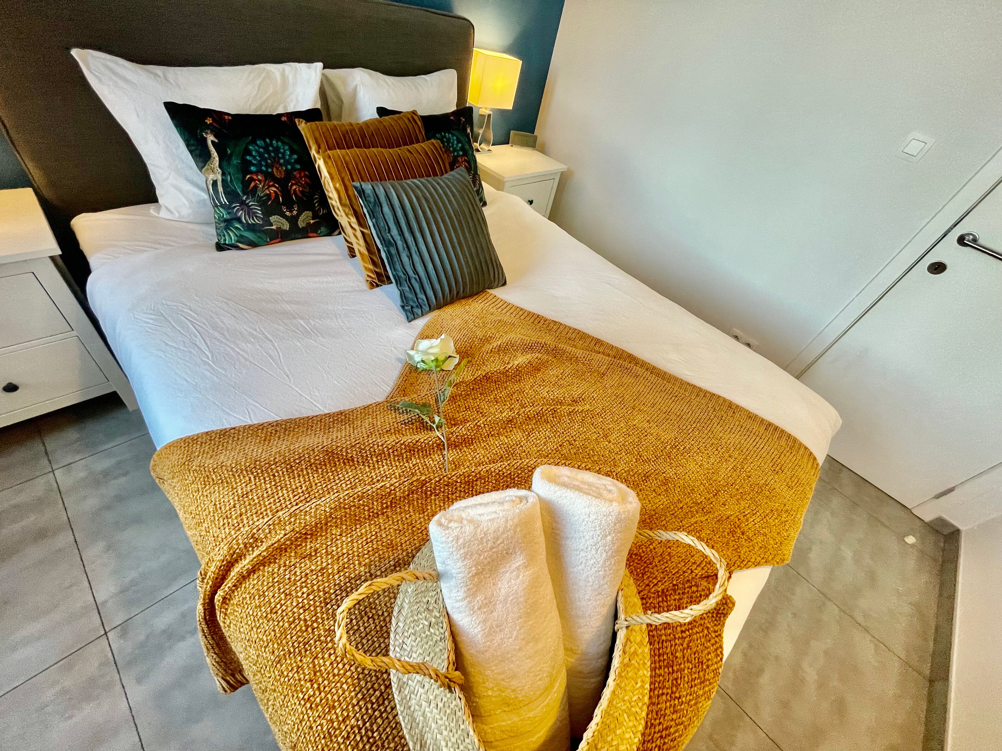 Una cama bien hecha con edredón blanco, una manta marrón y una almohada decorativa con diseño de jirafa.