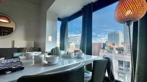 Un comedor moderno con un amplio ventanal, una mesa dispuesta con vajilla blanca y una planta de cactus.