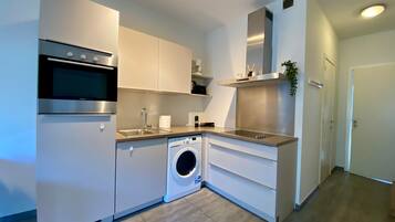 Cocina compacta con horno empotrado, lavadora y cafetera.