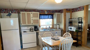 A compact kitchen with a refrigerator, stove, and microwave. There is a dining table with chairs and a window with curtains. - SPRING GETAWAY! Comfortable 2BR cozy cottage just a few steps from Sandusky Bay! (Sandusky)