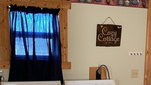 A laundry area with two white washers and dryers, a blue curtain, and a 'Cozy Cottage' sign on the wall. - SPRING GETAWAY! Comfortable 2BR cozy cottage just a few steps from Sandusky Bay! (Sandusky)