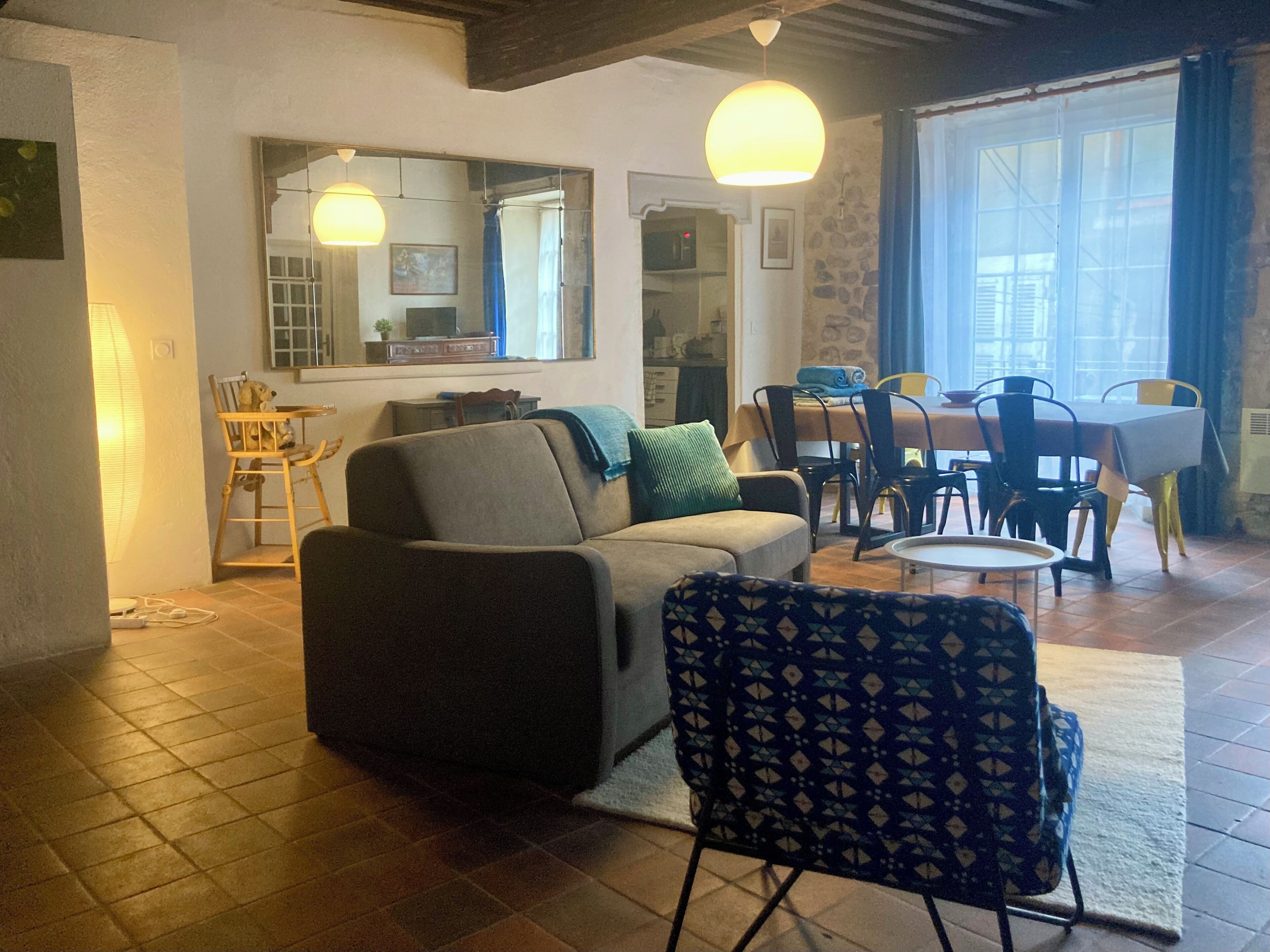 A living room with a sofa, patterned chair, dining table, and kitchen area visible through an open door.