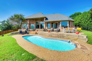 Ein Haus mit Garten, Swimmingpool, Terrassenmöbeln und einer Steinmauer.